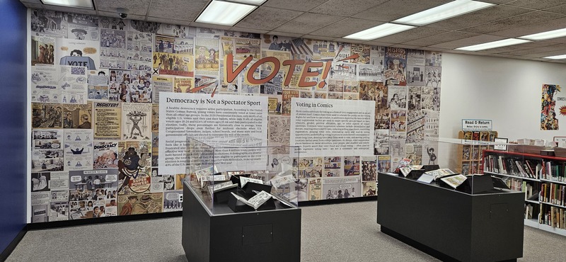 Image from the physical exhibit that shows display cases and wallpaper
