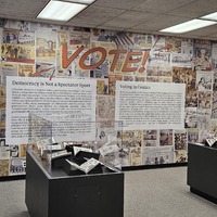 Image from the physical exhibit that shows display cases and wallpaper
